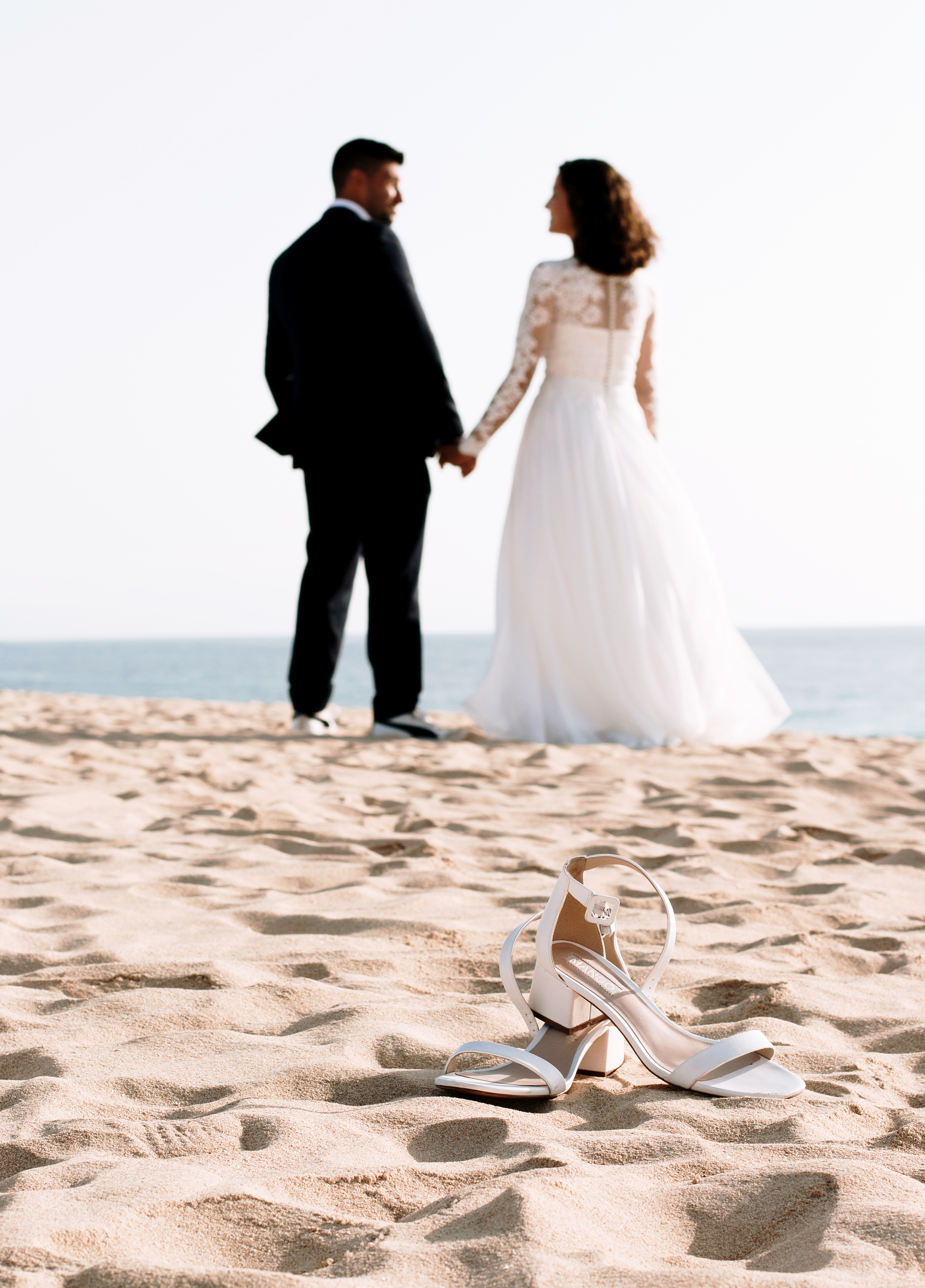 Bride's shoes are in the focus at the beach, couple stands more far away from shoes and they are blurry