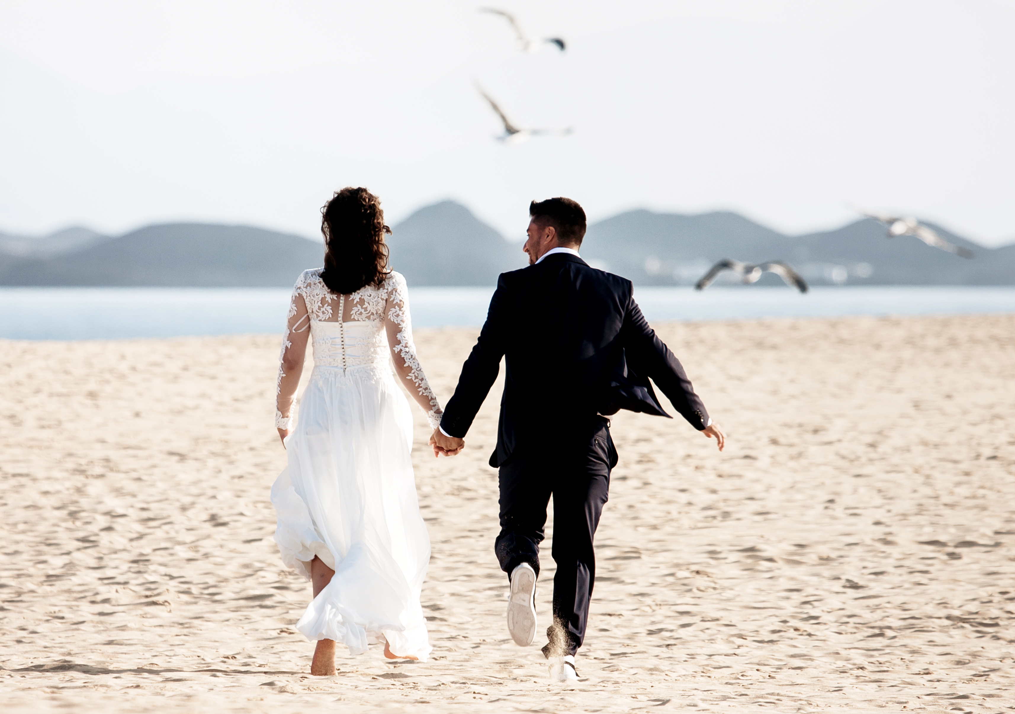 Bride and groom are running towords the beach of Grandes Playas in Fuerteventura