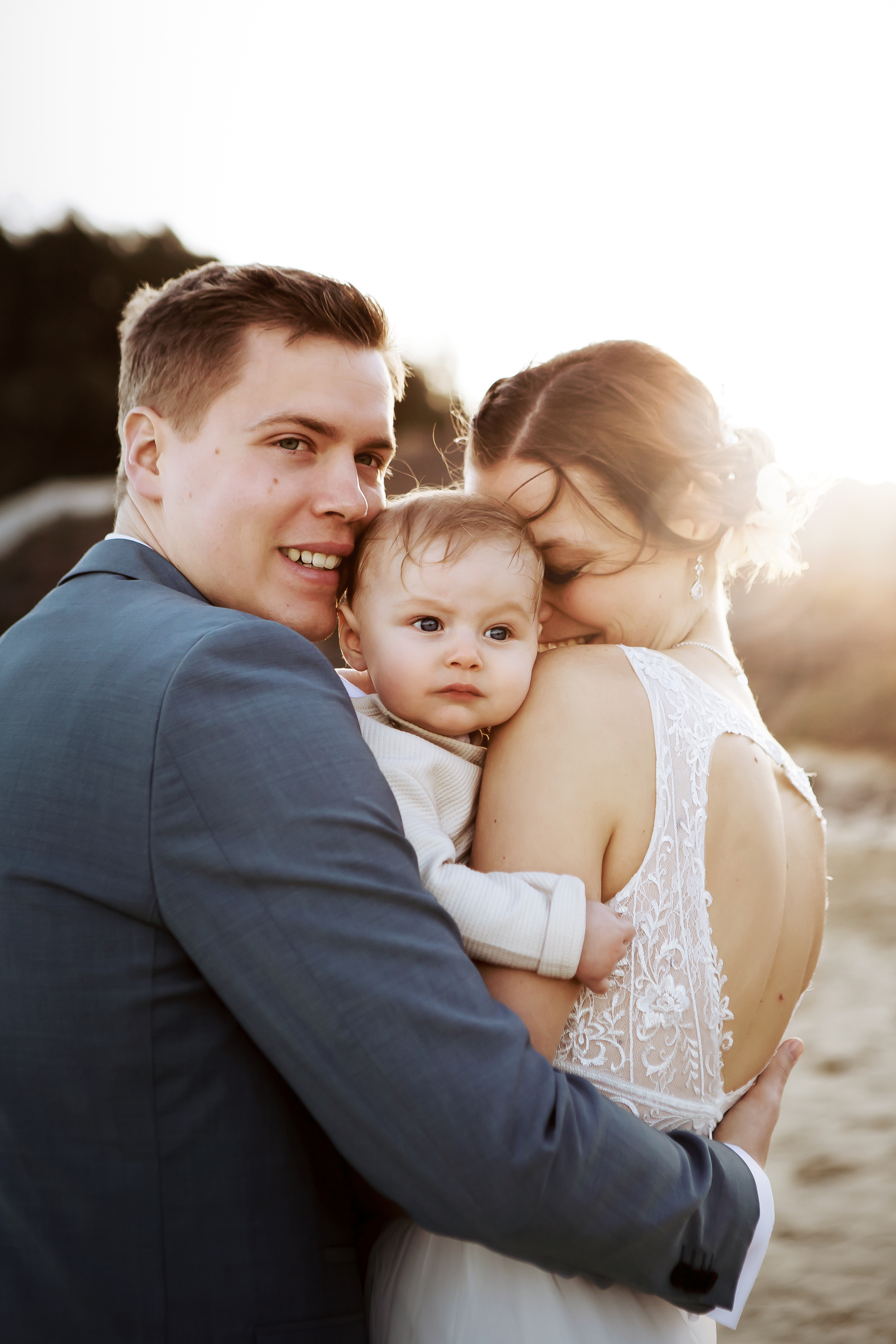 Newlyweds holding they baby on their hands in front of professional wedding photographer's camera