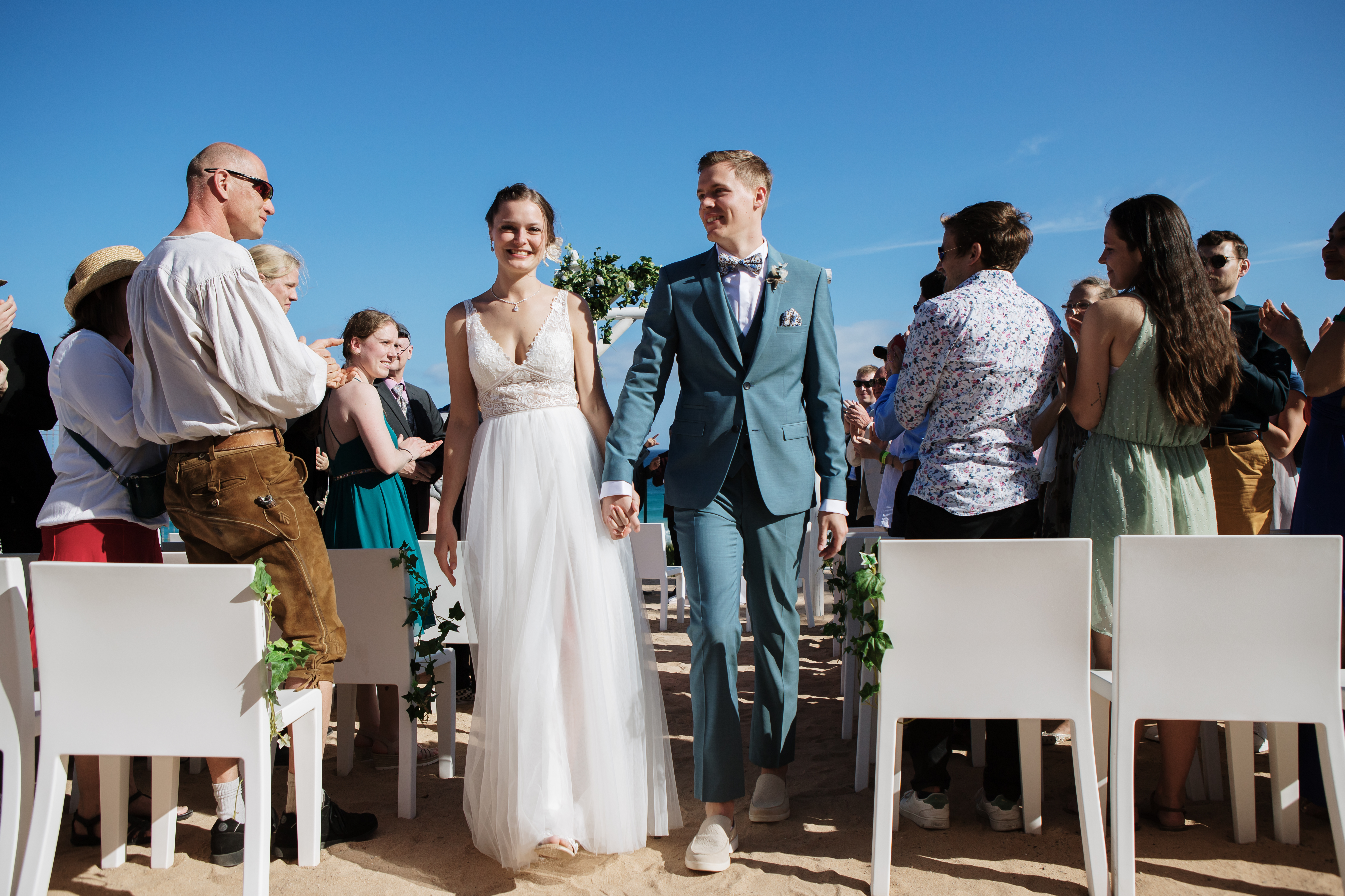 Unvergessliche Erinnerungen an Ihren Hochzeitstag in Fuerteventura durch professionelle Fotografie. Braut und Bräutigam verlassen ihre Zeremonie im Fuerteventura Princess Hotel in Esquinzo, während Gäste sie grüßen. Unser erfahrener Hochzeitsfotograf fängt die Magie des Moments ein, damit Sie ihn für immer in Erinnerung behalten können