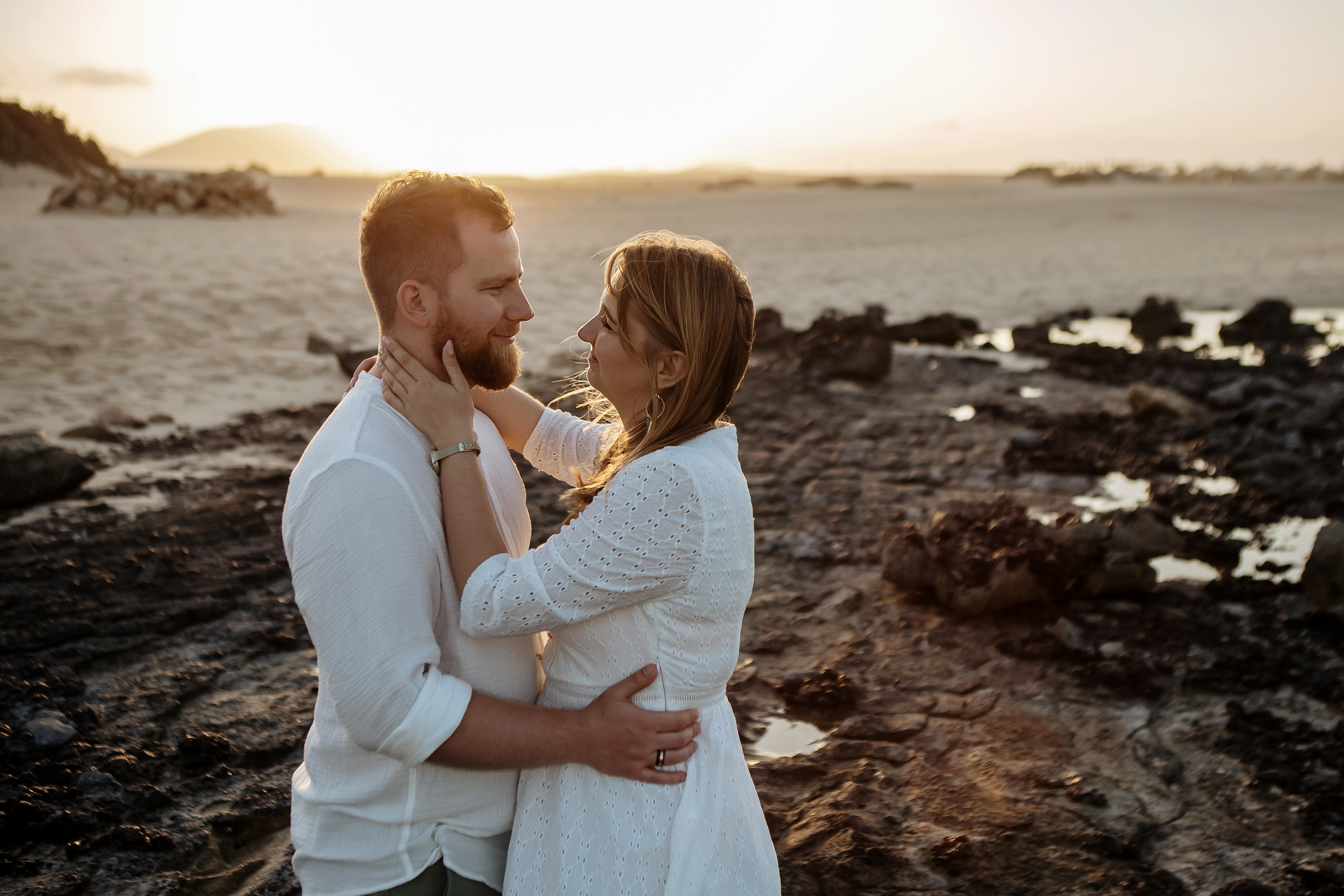 El sol está detrás de la pareja que se mira durante la hora dorada en las Dunas de Corralejo en Fuerteventura mientras el fotógrafo de bodas toma la foto