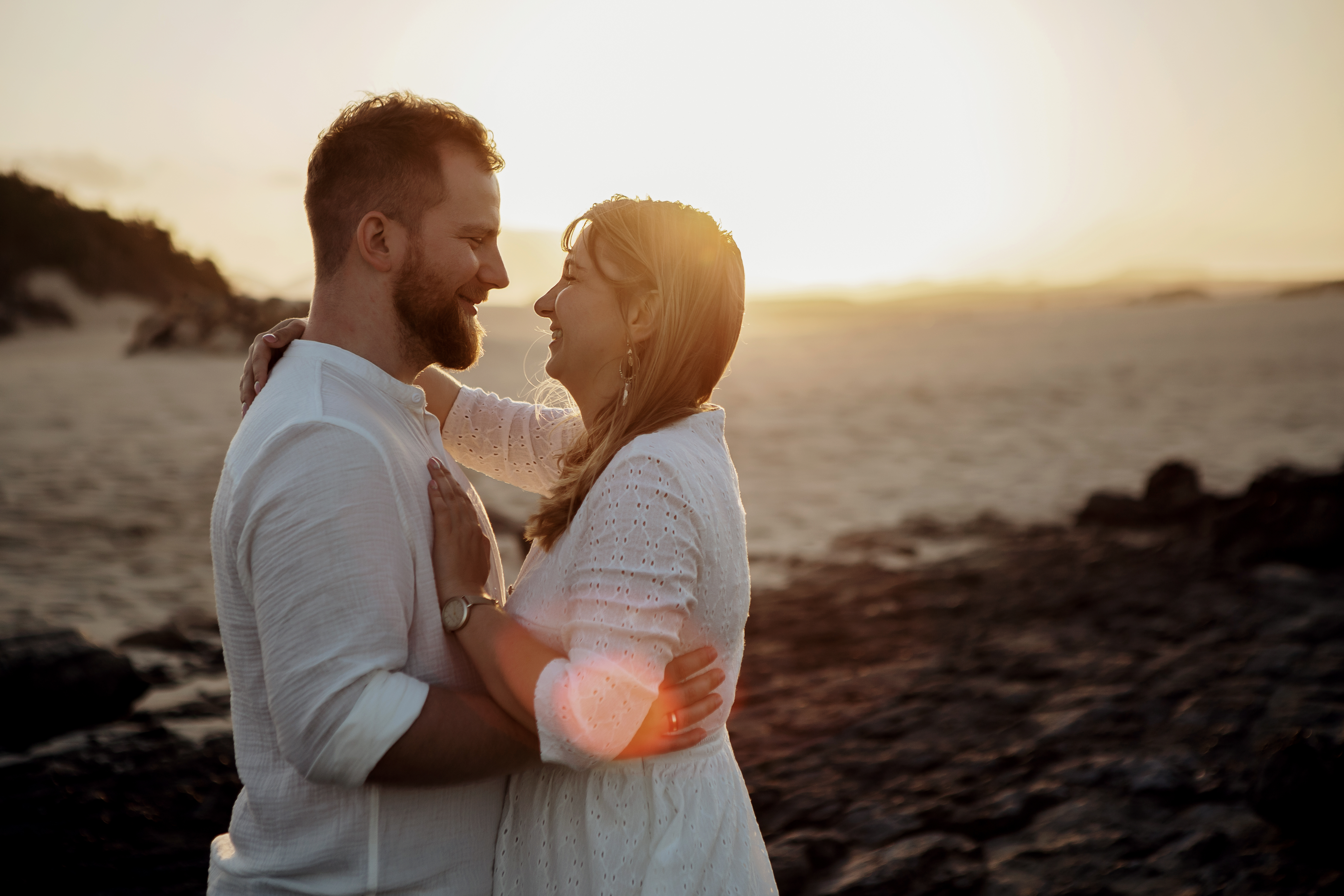 Die Sonne steht hinter dem Paar, das sich während der goldenen Stunde in den Dünen von Corralejo auf Fuerteventura ansieht, während der Hochzeitsfotograf das Foto macht