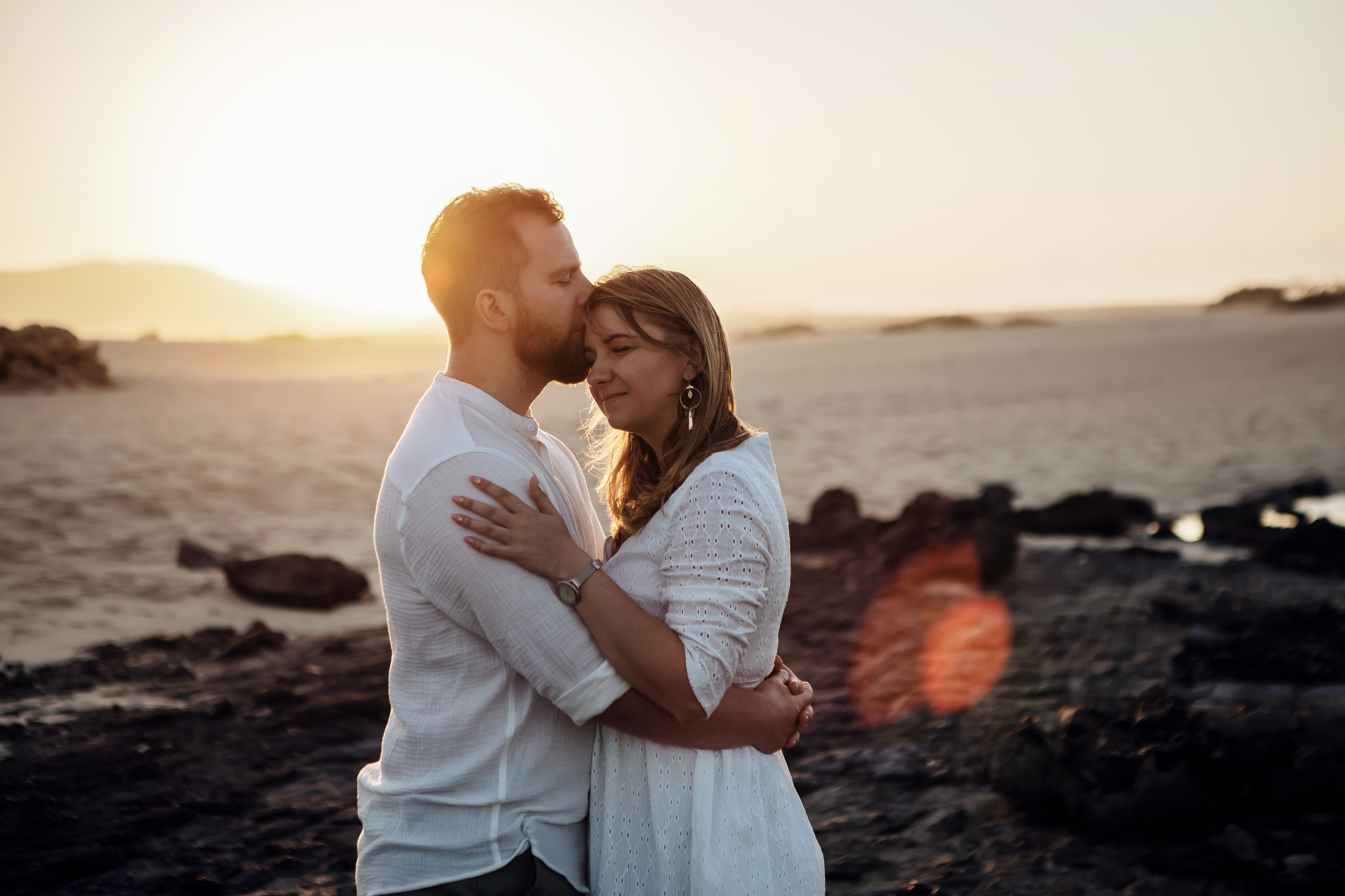 The sun is behind the couple which is looking to each other during golden hour in the Dunes of Corralejo in Fuerteventura while wedding photographer takes the picture